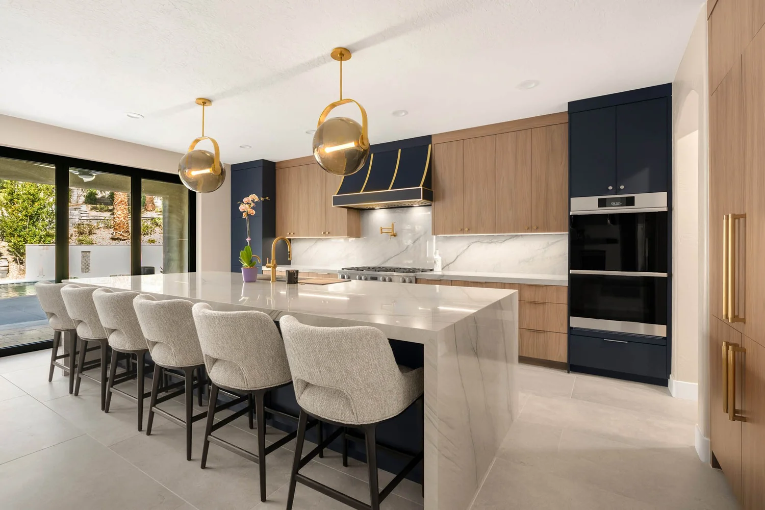 A Spot for Everyone kitchen — navy and white oak cabinetry with brass globe pendants and a six-seat island
