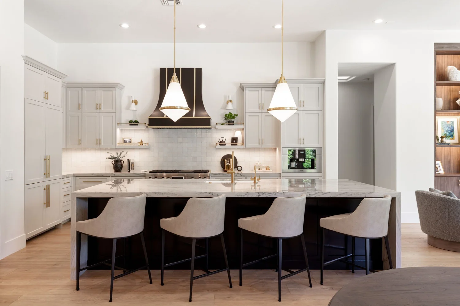 Maison des Papillons kitchen after — pale cabinetry, black-and-brass hood, gold pendants over a marble island