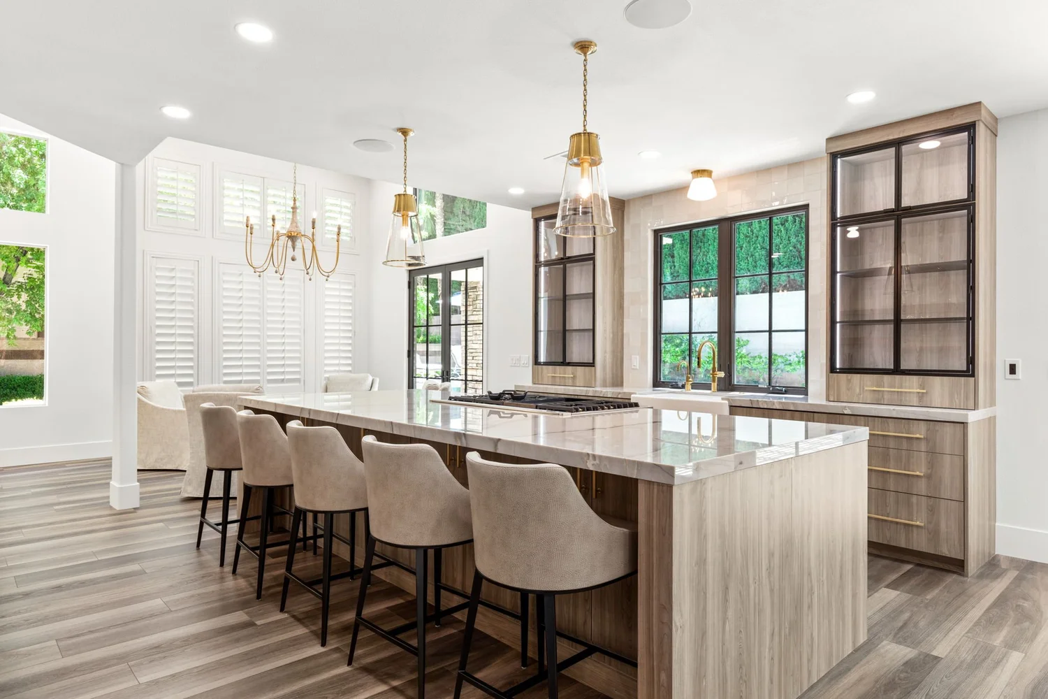 Forever Home kitchen after — long marble island with linen counter stools, brass pendants, plantation shutters