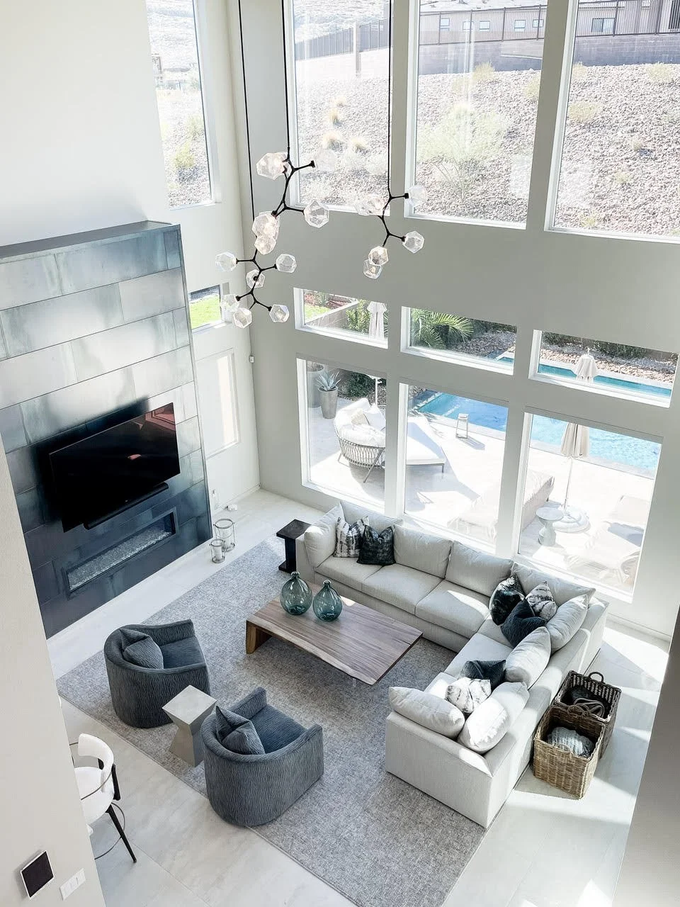 On the Rocks two-story living room — floor-to-ceiling windows over the pool, branch chandelier