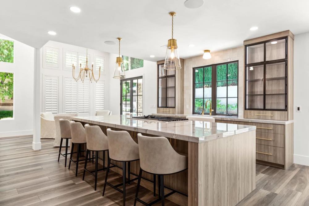 Forever Home kitchen after renovation by SK Design — long marble island, brass pendants, plantation shutters