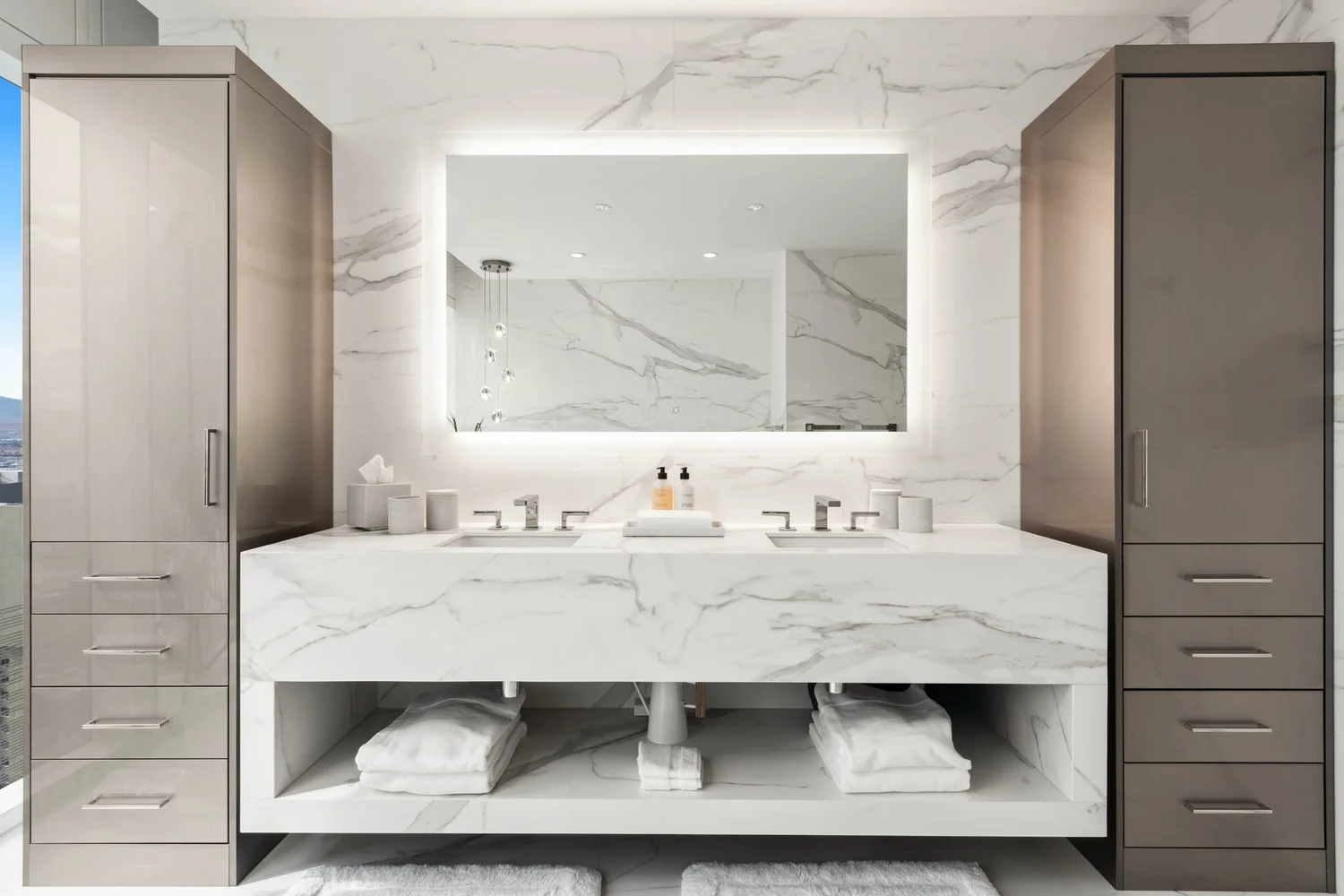 Raiders Den bath — book-matched marble vanity wall with double sinks and lit mirror